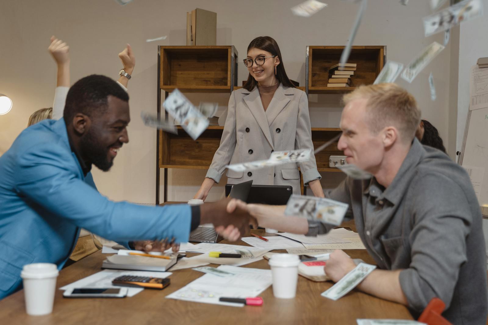 Joyful business colleagues celebrating a successful deal with handshake and flying money.
